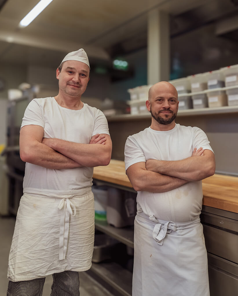 Zwei B&auml;cker in wei&szlig;er Kleidung stehen mit verschr&auml;nkten Armen in einer B&auml;ckerei